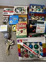 Overview of all included items on carpeted floor showing assortment of vintage Christmas ornaments, light sets, and tree stand.