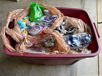Top view of large plastic storage bin filled with multiple small vintage McDonald's toys in sealed individual plastic bags separated by grocery bags.