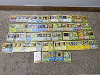 Wide shot of about 62 Japanese Pokemon cards laid out in rows on the carpet, showing original series and Team Rocket cards.