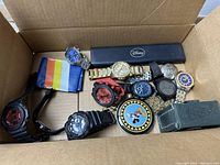 View of assorted watches including wristwatches with plastic, metal straps, and a Disney box.