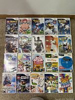 Photo shows 24 used Nintendo Wii game cases arranged on a carpet. Titles from various genres including action, puzzle, sports, and party games.