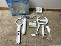 Photo showing all items including Sport Pack box, Wii Sports game case, controllers, charging station, accessories (tennis racket, baseball bat, golf club, steering wheel), and charging cables on carpet.