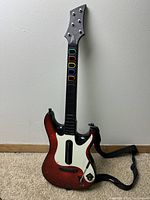 Front view of the wireless guitar controller showing red sparkle body, black neck with colored fret buttons, and strap.