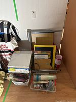 Overview of lot showing stacked art papers, light box, paintbrushes, cutters, and storage containers in a corner.