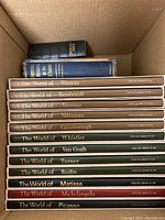 Top-down view of a box containing 15 hardcover art books from Time Life's The World of series including Watteau, Rembrandt, Vermeer; mostly tan spines.
