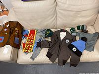 Full assortment of Boy Scouts uniforms and accessories on couch including jacket, vest, shorts, hats, socks, ribbons