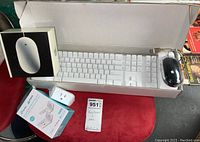 Full lot image showing Apple wired white keyboard in open box, Apple Pro black mouse in sealed plastic, and Kasa Smart Wi-Fi Plug Mini in retail box on red surface.