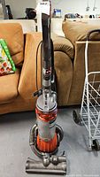 Front view of Dyson DC25 upright vacuum cleaner showing dust bin, handle and wheels.