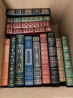 Top-down view of a cardboard box holding 14 leatherbound books arranged in two rows.