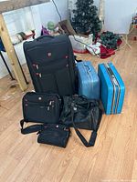 Full view of all bags grouped on floor including black Swiss Army bags and vintage blue luggage