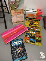 View of lot showing Matchbox car carrying case with several die-cast cars, original Matchbox box, Disneyland map packaging, and 'Understanding Comics' book