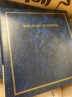Top view of the closed blue textured album with gold border and title 'THE STORY OF CANADA' on the cover.