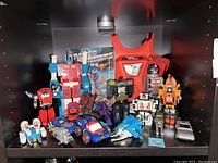 Shelf view showing entire group of G1 Transformers figures, stickerbook, chest plate and shampoo bottle.