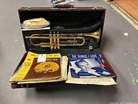 Brass trumpet in its case surrounded by sheet music pieces on a tabletop