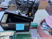 Portable Singer Featherweight model 221 sewing machine seated on its black metal case alongside a pink woven basket and other accessories