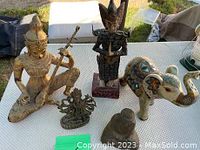 Overview photo showing all statues and figurines on a white textured surface outdoors.