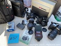 Overview of main lot items on table including two SLR cameras, lenses, flash unit, charger, memory card, manual and cases