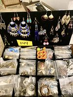 View of multiple pairs of earrings displayed on black stand with many more pairs in small plastic bags spread below the stand.