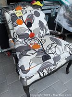 Full view of the living room chair showing black stained wood frame, patterned cushion and upholstery.