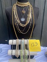 Full display of long necklaces on black bust and additional necklaces on white padded stand, showing mix of gold-tone, beads, and pendants
