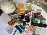 Office globe shown with various office supplies on white table: staplers, business card holders, tape dispensers, and other small items.