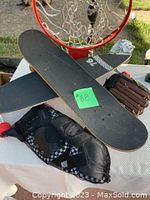 Longboard skateboard with black grip tape and red wheels, protective pads in mesh bag, and Rawlings baseball glove on table.