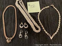 Full view of four necklaces and two pairs of earrings arranged on black background with lot number visible.