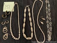 All items shown arranged on black cloth background, showing various sterling silver earrings and necklaces, some with beaded design and others with linked circle chain design.