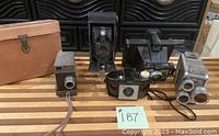 Overview of the five vintage cameras on a wooden surface with a leather camera case in background