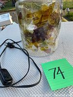 Full lamp showing cylindrical shape, glass shade with colored leaf patterns, electrical cord and switch.