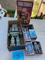 Overhead view of Star Strider AIJ-01 in box alongside three smaller boxed robots on table outdoors