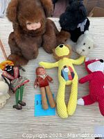 Wide shot of all items arranged on fabric surface showing entire lot: baby doll, plush bears, knit figures, toy figurine, and monkey doll.