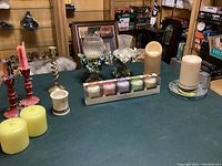 Overview of various candlesticks, pillar candles, LED candle, Yankee Candle aromatherapy candle set, and floral glass candle holders on green table.