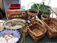 Photo showing 6 Christmas baskets, 2 serving trays with Christmas designs, dried gold artificial flowers, and a package of gift wrapping shreds.