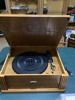Front and slightly angled view of the Crosley Turntable CR47 with wooden lid open, showing the black platter and attached tonearm with cartridge and stylus, wood grain finish visible.