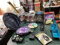 Wide view of all items in the lot on a surface including projection lights in boxes, timers, walkie talkies, cutters, and household items.