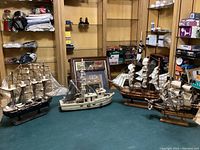 Photo showing four model ships on a table in a room with shelving and various household items in the background.