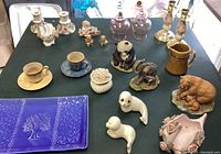Top-down photo of all porcelain and ceramic items on a black surface showing various animal figurines, teacups, candlesticks, trinket box, and commemorative plate.