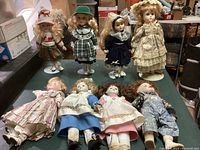 View of eight small porcelain dolls displayed on a flat surface, showing varying vintage-style clothing and details for identification.