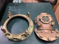 Top down view on table of round metal porthole frame and vintage style brass diving helmet sculpture side by side.