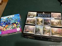 Both the Thomas Kinkaid 10-pack jigsaw puzzles and the separate Harmony Dolphin 550-piece puzzle shown side by side.