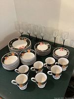 Photo showing entire china set including cups, bowls, plates, and wine glasses arranged on table against a wall.