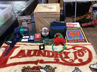 Photo showing full lot including star shower projector, laundry rug, elf hair band, CDs case, dog collar, decks of cards, books, note holder, vase, wooden box, money clip, and beer mug.