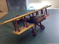 Photo of tin biplane model on green surface showing the front, wings, propeller, and wheels.