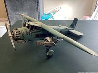 Angled front-side view of a large tin airplane model showing propeller, cockpit, and side windows with worn blue paint.