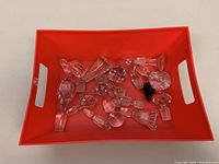 Top view of more than 15 assorted clear and one dark glass bottle stoppers in a red tray showing variety of shapes and sizes.