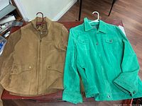 Both jackets laid flat side by side showing beige jacket and green jacket