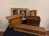 Photo showing three wooden boxes and three framed copper wall art pieces arranged on a black surface against a white wall, showing wear on wood and frames.
