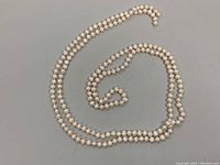 Full length of the 64 inch pearl necklace laid out in a loop shape on a flat gray surface.
