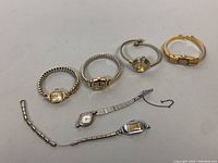 Full view of six vintage ladies watches arranged on a white surface showing different band styles and case shapes.